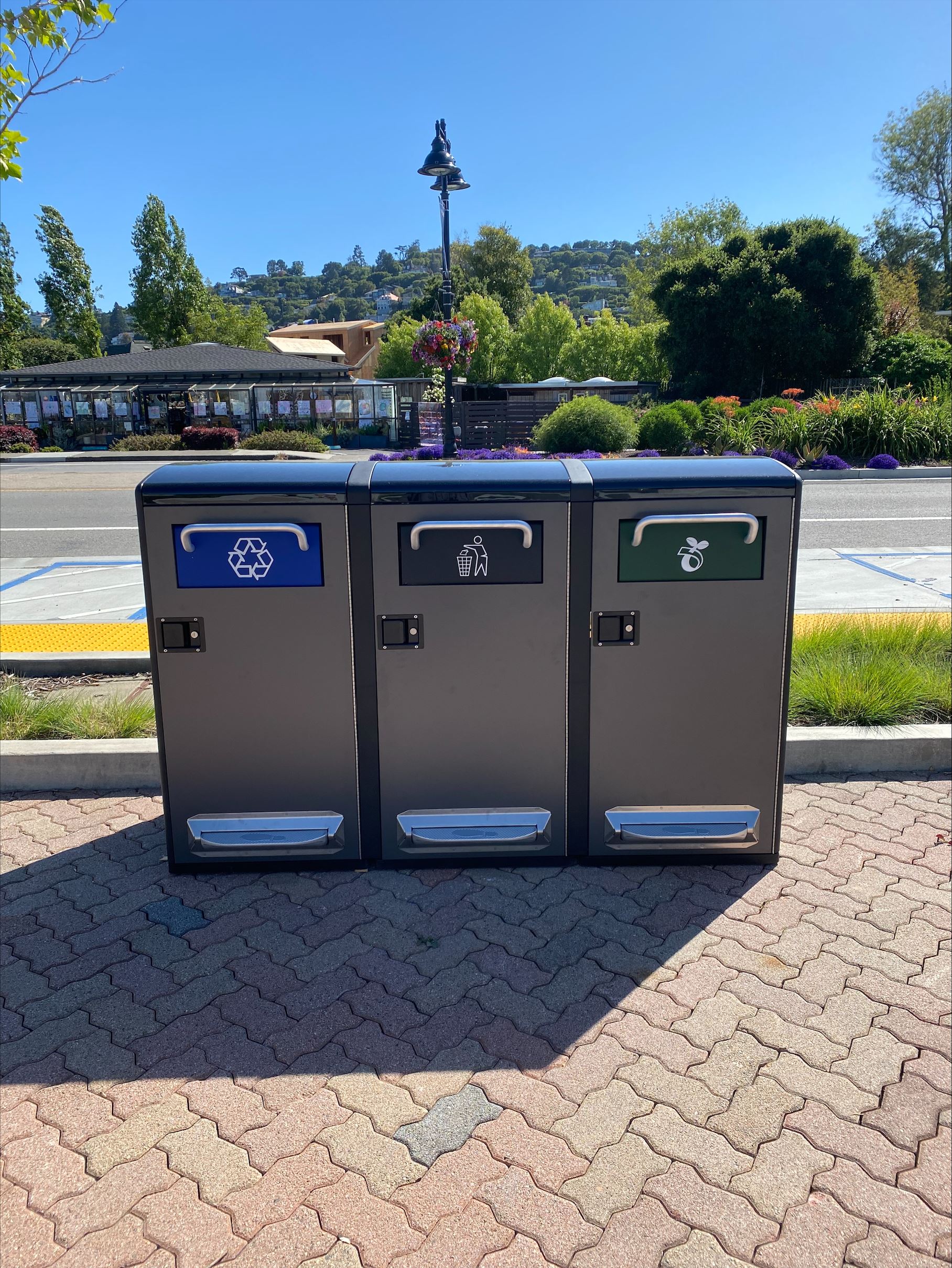 three new waste receptacles for landfill recycling and compost sit next to the street in front of th