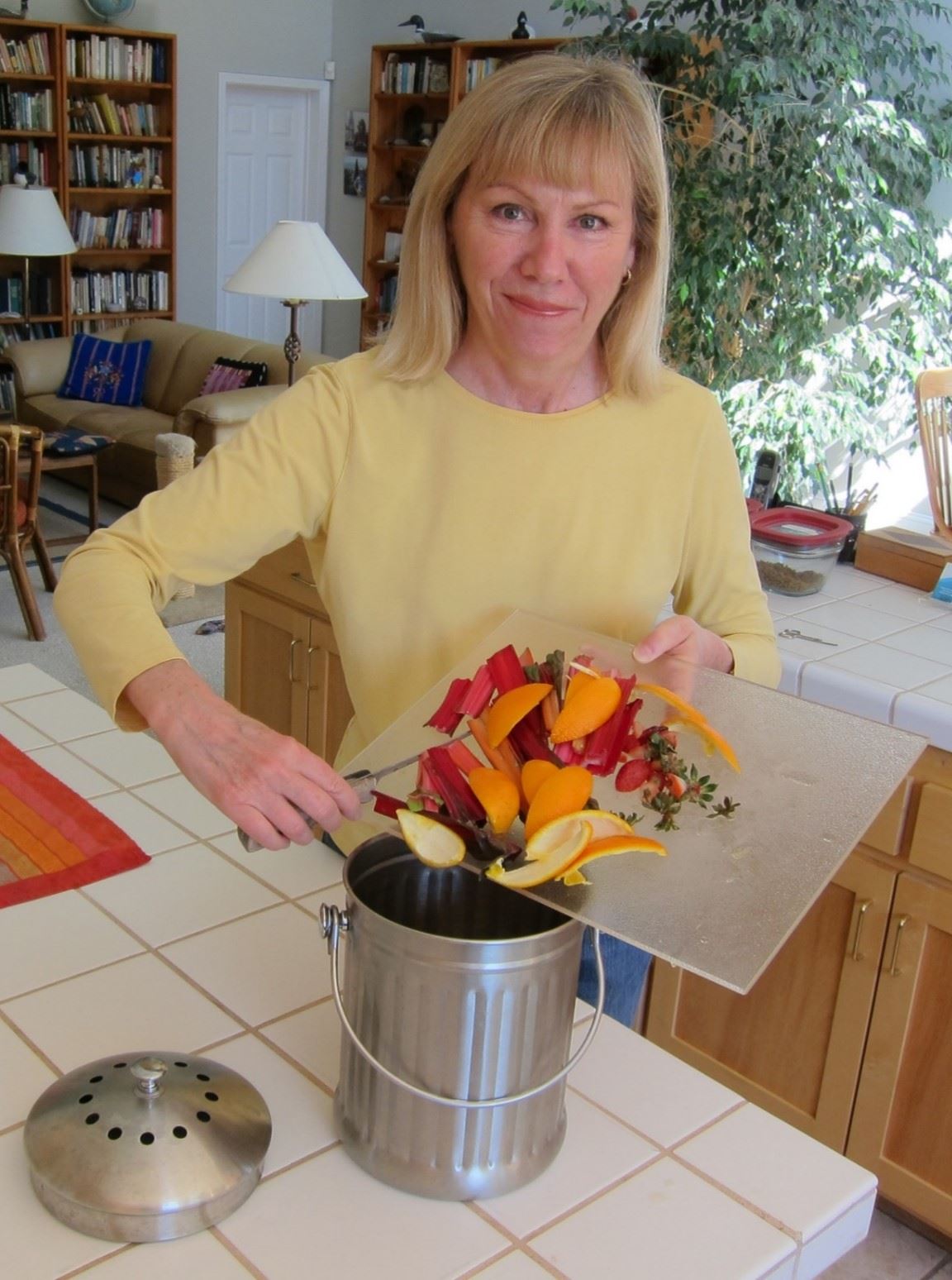 Woman in kitchen dumping food scraps into countertop compost bin